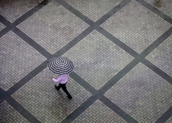 Office worker holding an umbrella walks out of a commercial building as it rains in