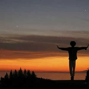 A man balances on a fence post as he watches the sun set over the Pacific Ocean in Santa Monica
