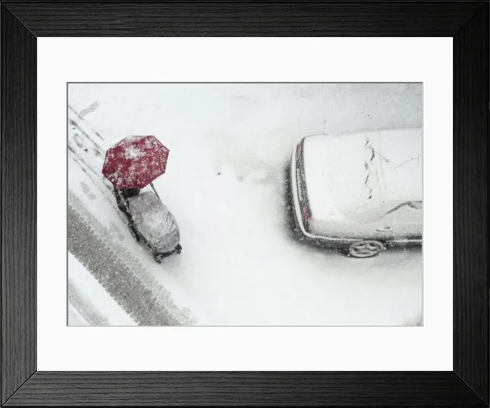 Framed Print : A woman pushes her child in a pram, while walking under an umbrella during heavy snowfall Framed Print : A woman pushes her child in a pram, while walking under an umbrella during heavy snowfall