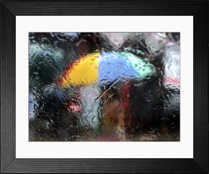Framed Print : A woman walking with an umbrella is seen from a window as it rains during the monsoon