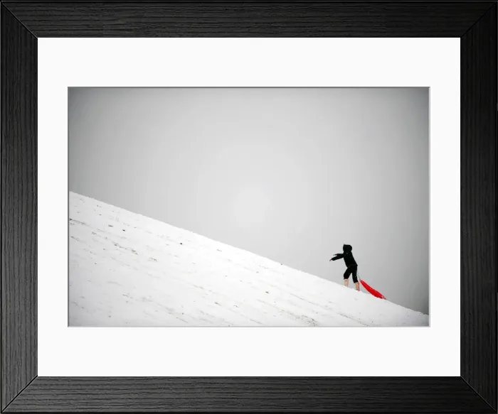 Framed Print : A child climbs a hill while sledging in the snow in London