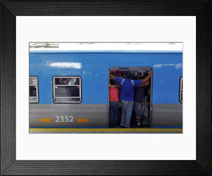 Framed Print : Passengers stand on the edge of a commuter train door at the Once train station in