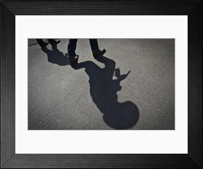 Framed Print : The shadow of a gunfighter is cast on the asphalt as competitors practice prior to