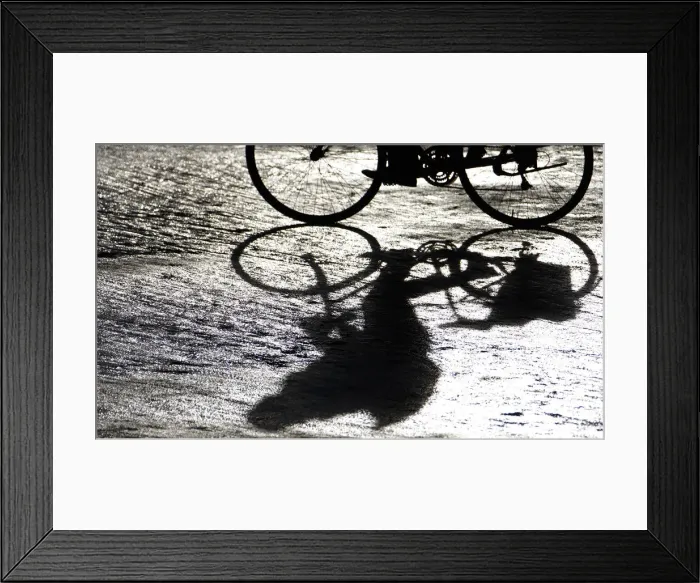 Framed Print : A man casts a shadow as he rides his bicycle Framed Print : A man casts a shadow as he rides his bicycle