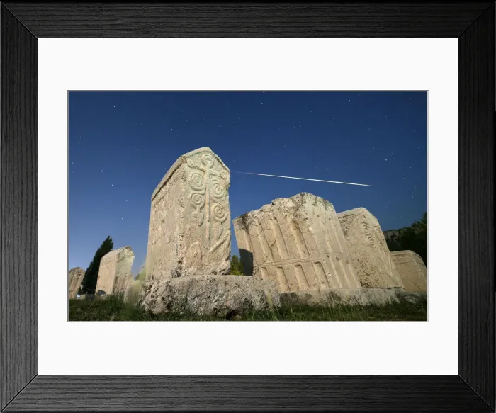 Framed Print : A meteor streaks past stars in the night sky above medieval tombstones during