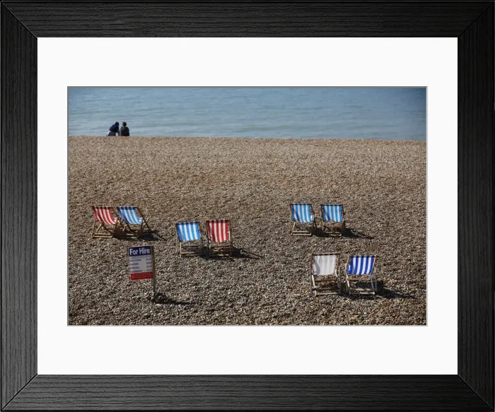 Framed Print : A couple sit on the beach near deck chairs in the sunny weather on Brighton beach Framed Print : A couple sit on the beach near deck chairs in the sunny weather on Brighton beach