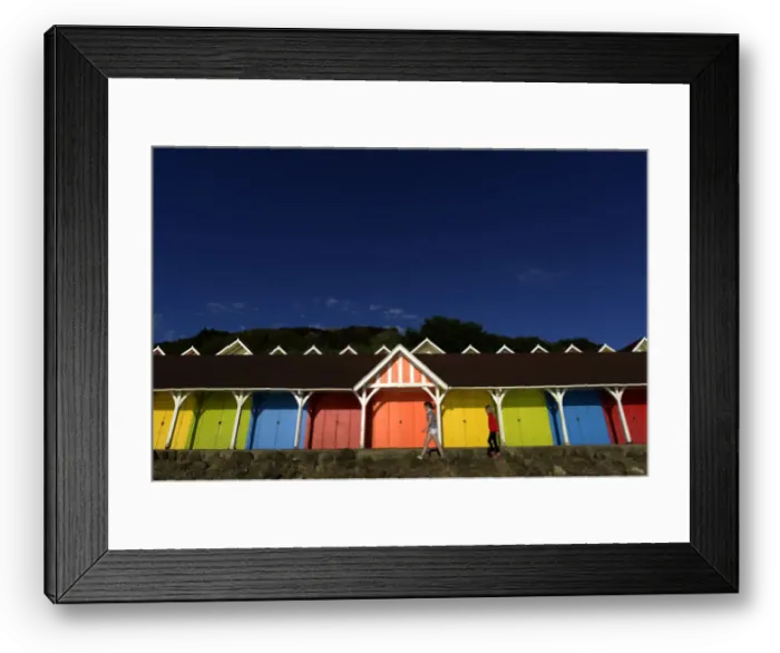 Framed Print : Two girls walk past beach huts in the North Bay in Scarborough