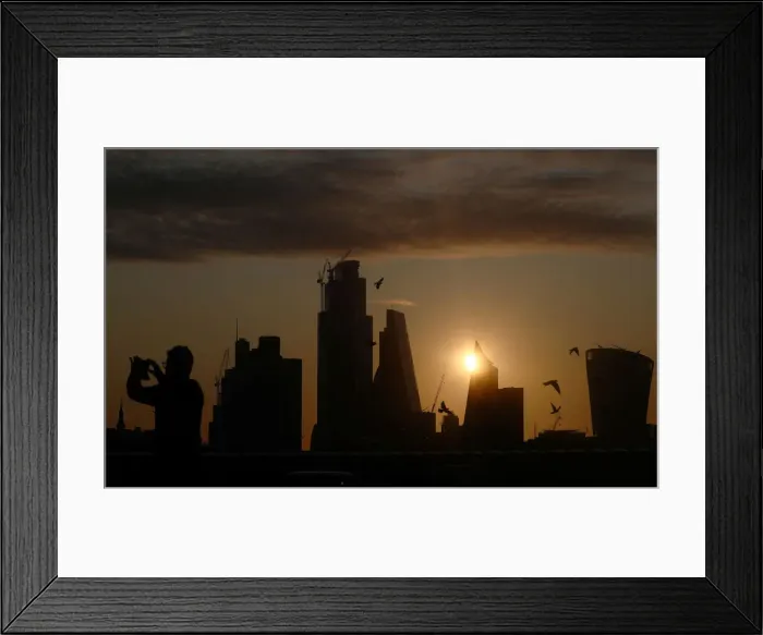 Framed Print : A man takes a photograph of the skyline as the sun rises behind the city of London Framed Print : A man takes a photograph of the skyline as the sun rises behind the city of London