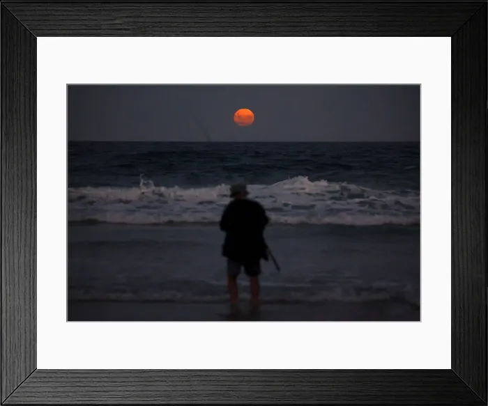Framed Print : A fisherman prepares to cast his line standing in the surf as a full moon rises Framed Print : A fisherman prepares to cast his line standing in the surf as a full moon rises