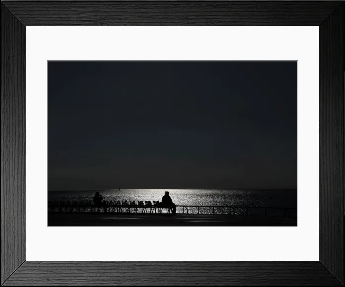 Framed Print : Sunlight reflects on the waters surface as people sit on chairs on a warm Framed Print : Sunlight reflects on the waters surface as people sit on chairs on a warm