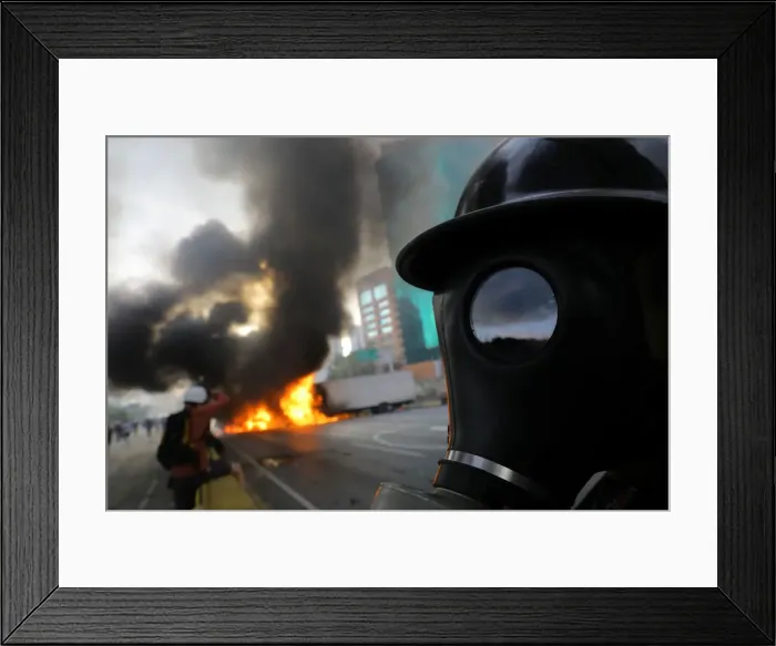 Framed Print : Demonstrators stand near burning trucks while rallying against President Nicolas Maduro