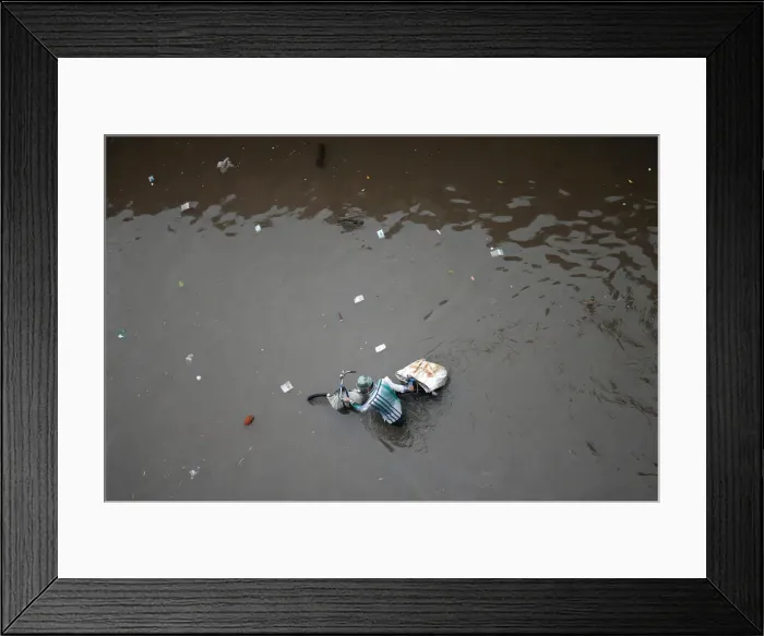 Framed Print : A man pushes his bicycle through a water-logged street after heavy rains in Ahmedabad