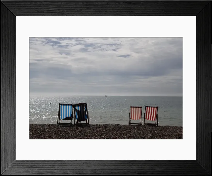 Framed Print : A woman sunbathes in a deckchair by the sea on a sunny day on Brighton Beach in southern