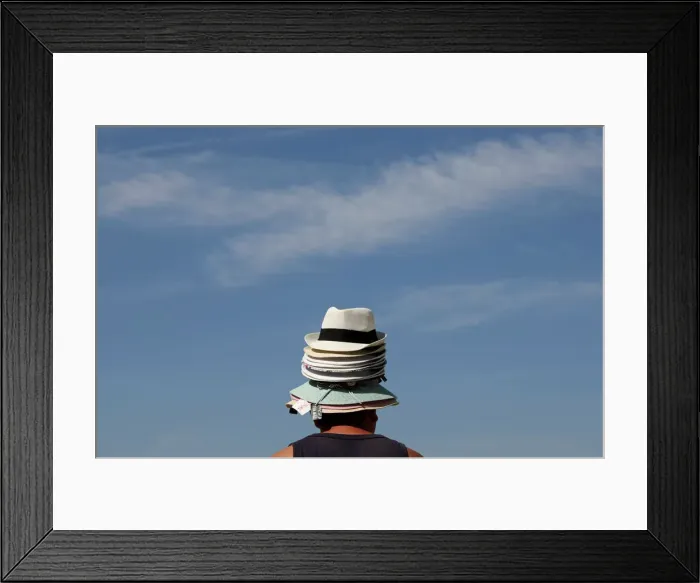 Framed Print : A hat seller wears his merchandise on his head as he tries to sell hats to tourists