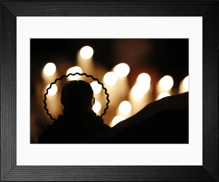Framed Print : Candles are seen lit behind a religious statue in front of which relatives pray for Framed Print : Candles are seen lit behind a religious statue in front of which relatives pray for