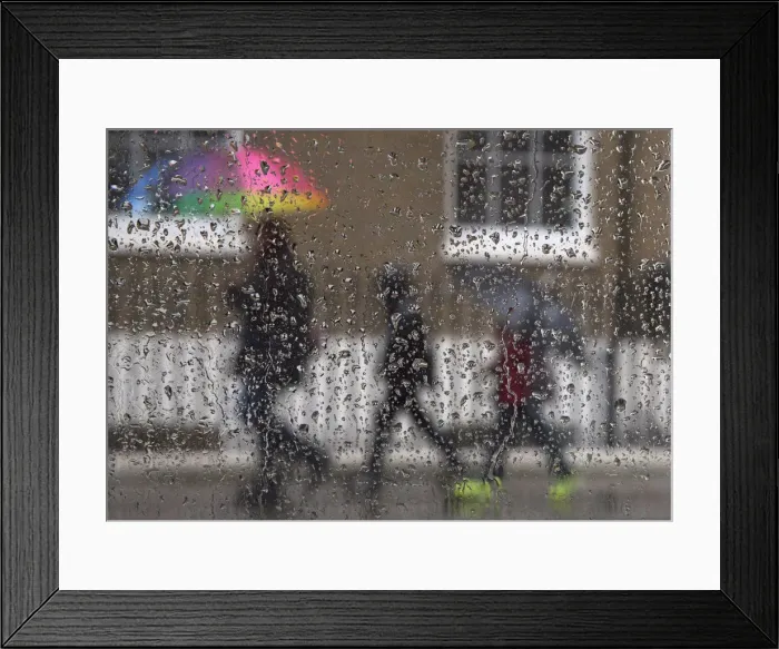 Framed Print : Family is seen through raindrops on a window as they shelter under umbrellas during a Framed Print : Family is seen through raindrops on a window as they shelter under umbrellas during a