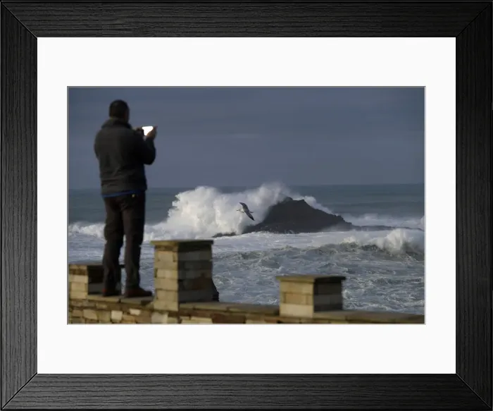 Framed Print : A man takes pictures of waves as they crash against a lighthouse in the port town of Framed Print : A man takes pictures of waves as they crash against a lighthouse in the port town of