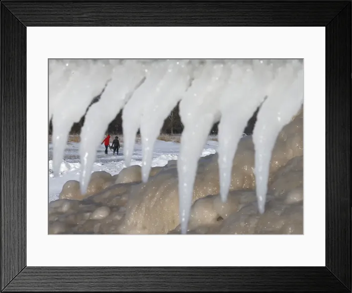Framed Print : Two women are framed by icicles and mounds of frozen ice as they walk along a beach in Framed Print : Two women are framed by icicles and mounds of frozen ice as they walk along a beach in