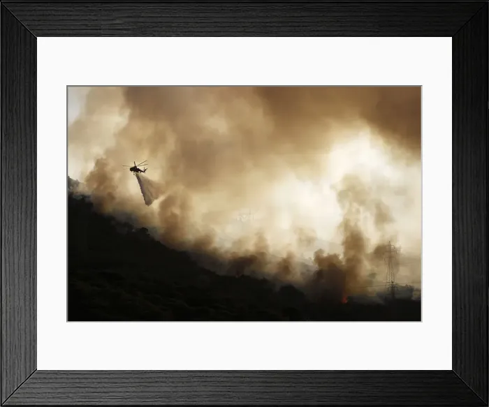 Framed Print : A firefighting helicopter drops water over a forest fire near Keratea