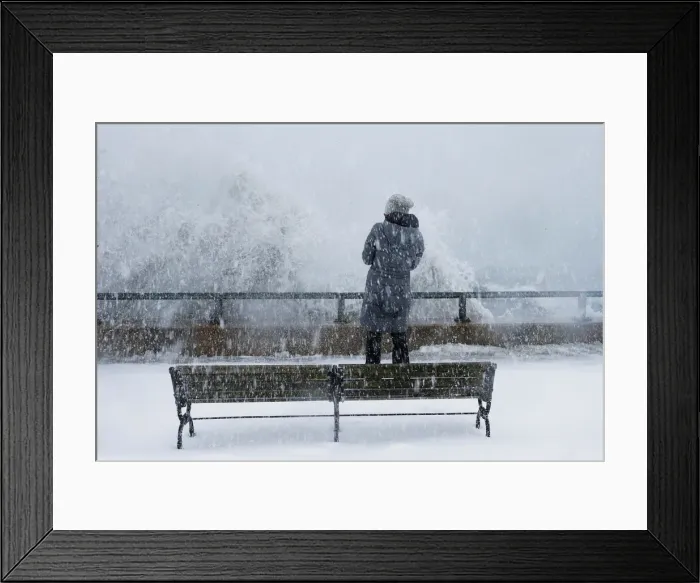 Framed Print : A woman watches as ocean waves overtop the seawall during a winter snow storm in
