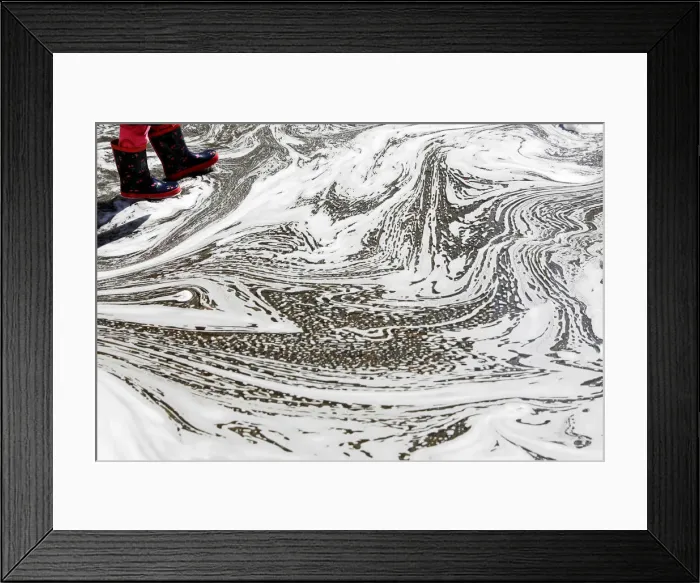 Framed Print : The boots of a young girl are seen in a puddle caused by melted snow at Madison Square