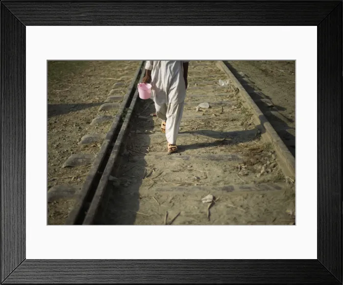 Framed Print : Flood victim carries a bucket while walking on a railway next to a relief camp in