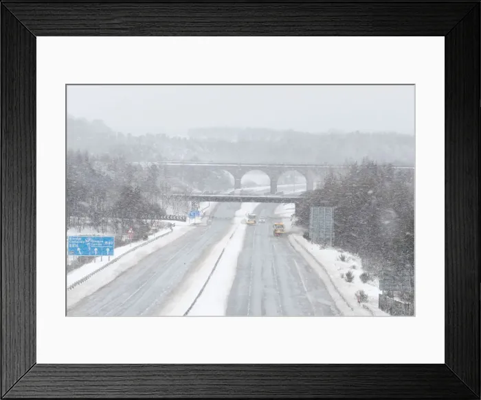 Framed Print : Snowploughs work on the M80 motorway after it was closed to clear vehicles stranded by Framed Print : Snowploughs work on the M80 motorway after it was closed to clear vehicles stranded by