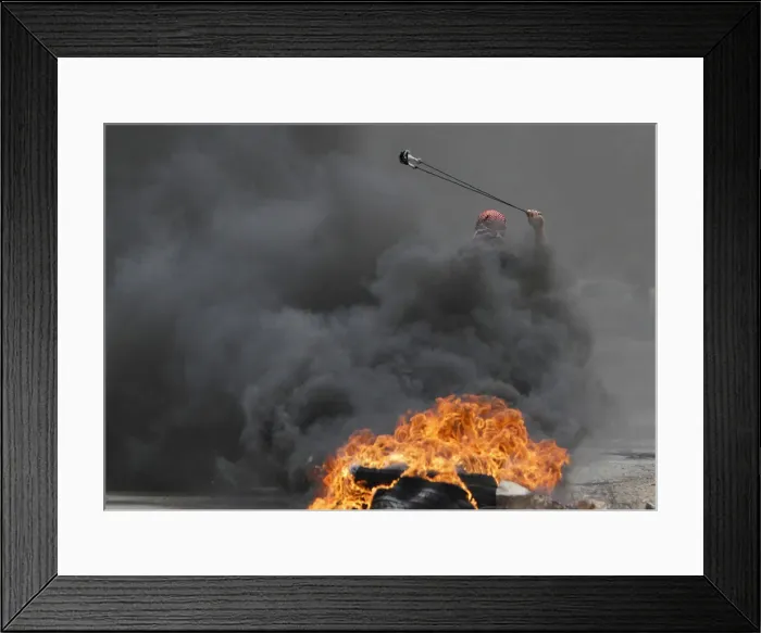 Framed Print : A Palestinian protester uses a sling to hurl stones towards Israeli troops during clashes Framed Print : A Palestinian protester uses a sling to hurl stones towards Israeli troops during clashes