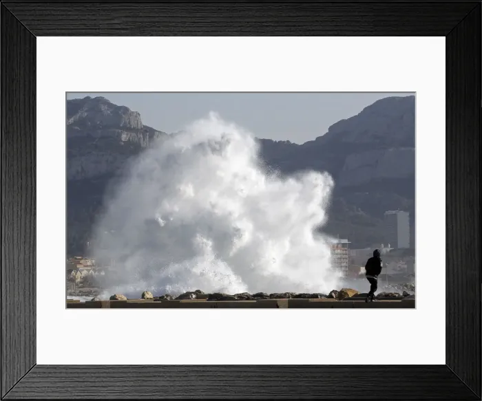 Framed Print : A passer-by walks as a high wave hits the waterfront in Marseille