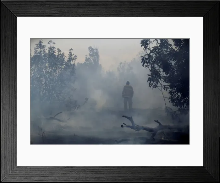 Framed Print : A firefighter tries to extinguish fire on the Israeli side of the border fence between Framed Print : A firefighter tries to extinguish fire on the Israeli side of the border fence between