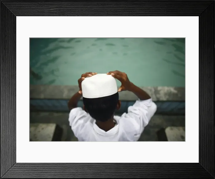 Framed Print : A Muslim boy puts on his hat after washing his face prior to Eid al-Fitr prayers Framed Print : A Muslim boy puts on his hat after washing his face prior to Eid al-Fitr prayers