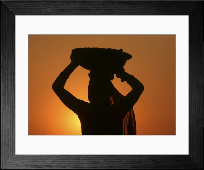 Framed Print : A woman labourer carrying cement is silhouetted against the setting sun at the site of a Framed Print : A woman labourer carrying cement is silhouetted against the setting sun at the site of a