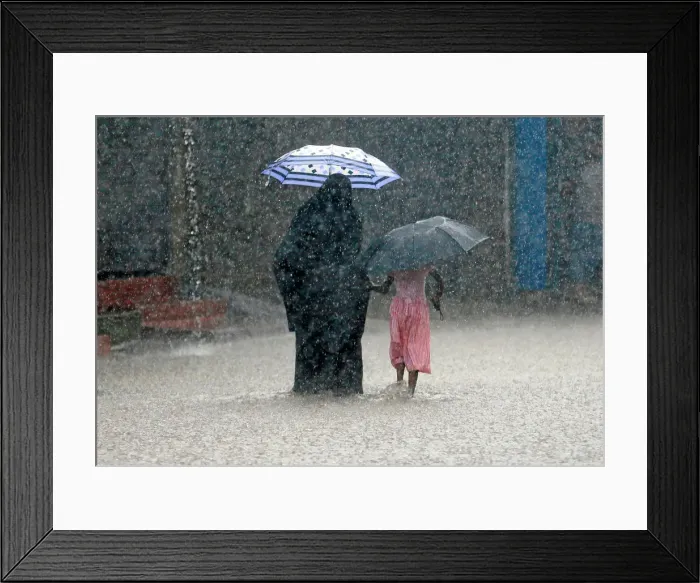 Framed Print : A woman walks with a girl along a flooded road in the heavy rains in Malwana Framed Print : A woman walks with a girl along a flooded road in the heavy rains in Malwana