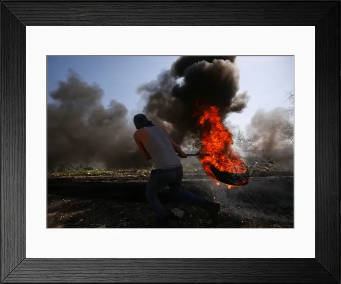 Framed Print : Palestinian protester moves a burning tyre during clashes with Israeli troops following a Framed Print : Palestinian protester moves a burning tyre during clashes with Israeli troops following a