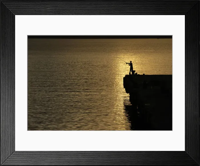 Framed Print : A man is silhouetted as he fishes on a pier at Uleelheu port in Banda Aceh