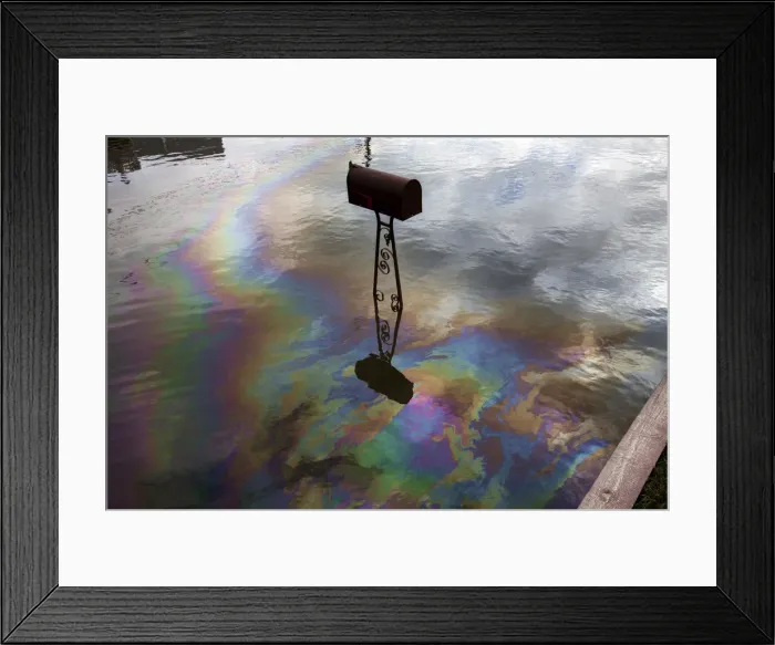Framed Print : A sheen caused by spilled fuel shines on water left in a street by the storm surge of
