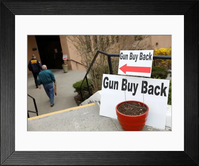 Framed Print : A man walks with his firearm during a community gun buy-back program in White Plains