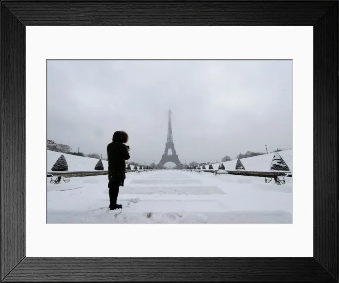 Framed Print : A woman takes pictures of the Eiffel Tower in Paris under the falling snow as winter Framed Print : A woman takes pictures of the Eiffel Tower in Paris under the falling snow as winter