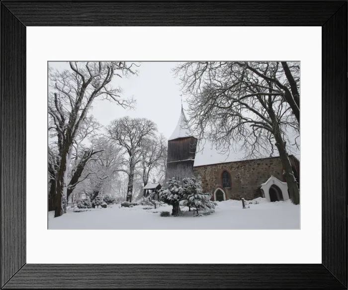 Framed Print : Snow covers the trees in the cemetery of a church in the village of Dersekow in northern