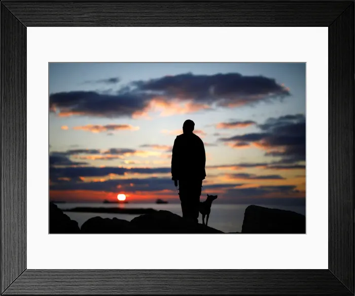 Framed Print : A man watches the sunset with his dog on a breakwater, along the shore of