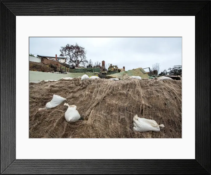Framed Print : Sandbags and webbing are seen on a small hill in front of a house burned to the ground in