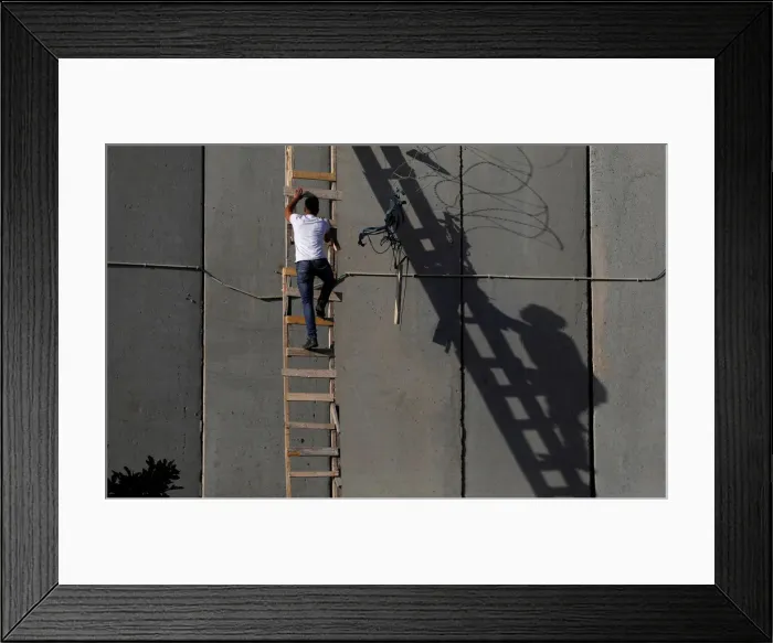 Framed Print : Palestinian uses a ladder to climb over a section of the controversial Israeli barrier Framed Print : Palestinian uses a ladder to climb over a section of the controversial Israeli barrier