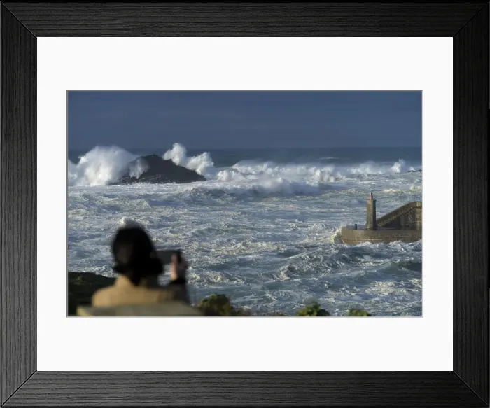 Framed Print : A woman takes pictures of waves as they crash against a lighthouse in the port town of