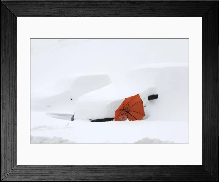 Framed Print : An abandoned red umbrella is supported by two cars covered in snow in the village of