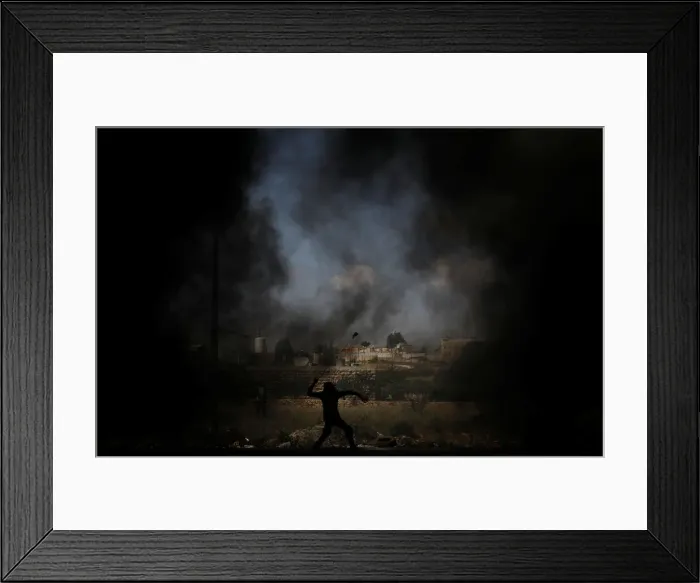 Framed Print : Palestinian demonstrator uses a sling to hurl stones at Israeli troops during a protest