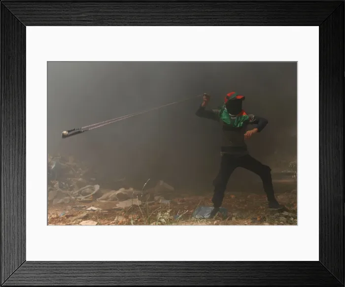 Framed Print : Palestinian demonstrator uses a sling to hurl stones at Israeli troops during a protest Framed Print : Palestinian demonstrator uses a sling to hurl stones at Israeli troops during a protest
