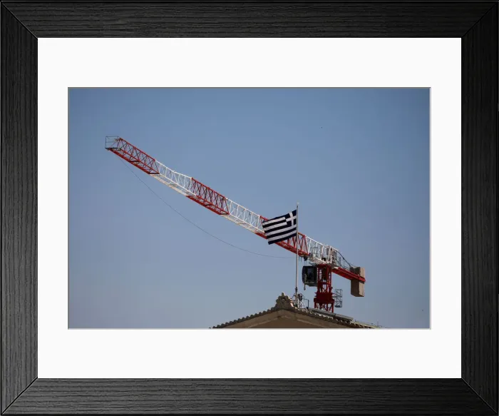 Framed Print : A Greek national flag flutters atop the parliament building as a construction crane is Framed Print : A Greek national flag flutters atop the parliament building as a construction crane is