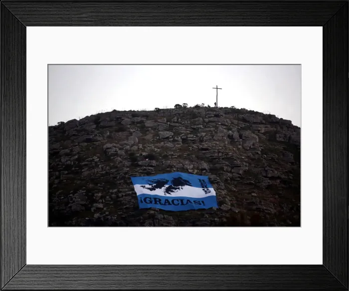 Framed Print : A man stands next to a cross as an Argentine national flag with an image of the Falkland Framed Print : A man stands next to a cross as an Argentine national flag with an image of the Falkland