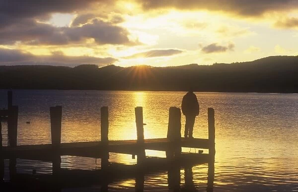 A man on a jetty on Coniston Water in the Lake District at sunset, UK