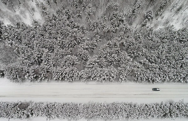 An aerial view shows a car driving along a forest road after snowfall outside Krasnoyarsk